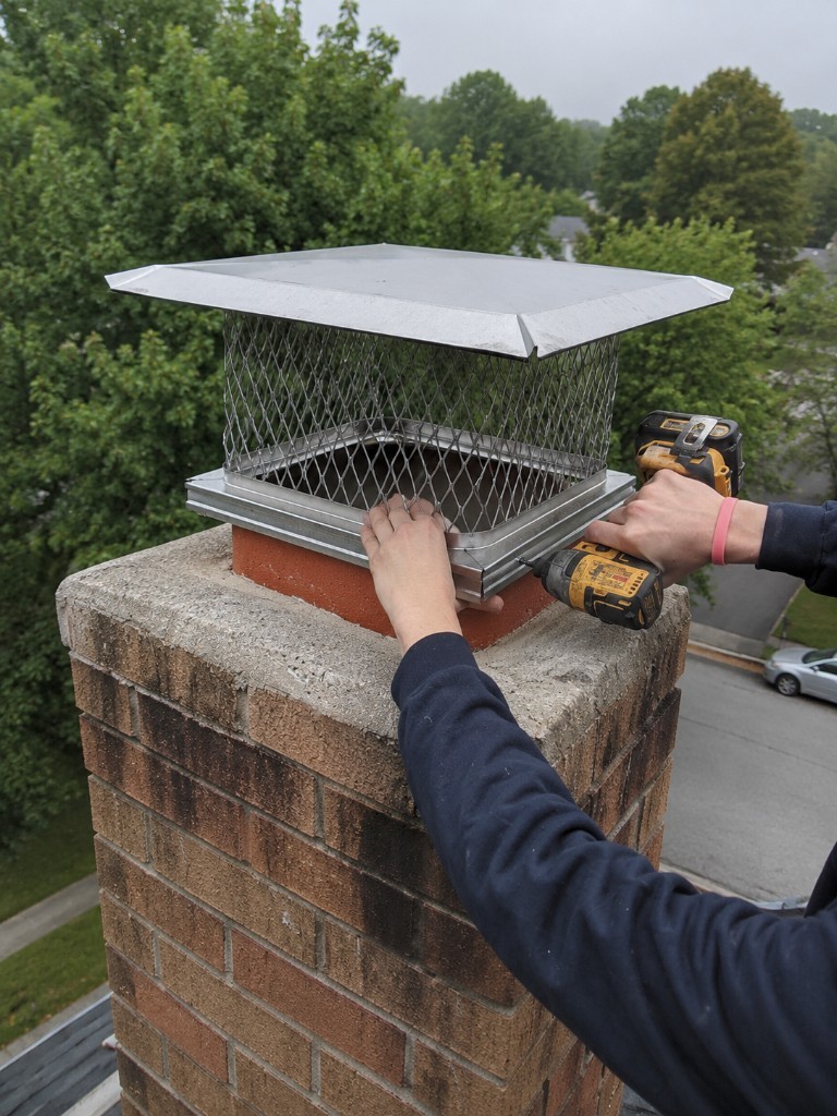 Technician securing a chimney cap on brick