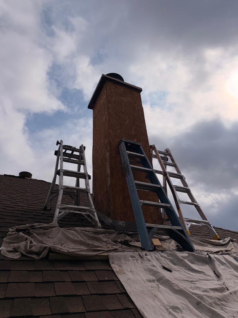 Chimney on a shingle roof under repair with ladders and a drop cloth