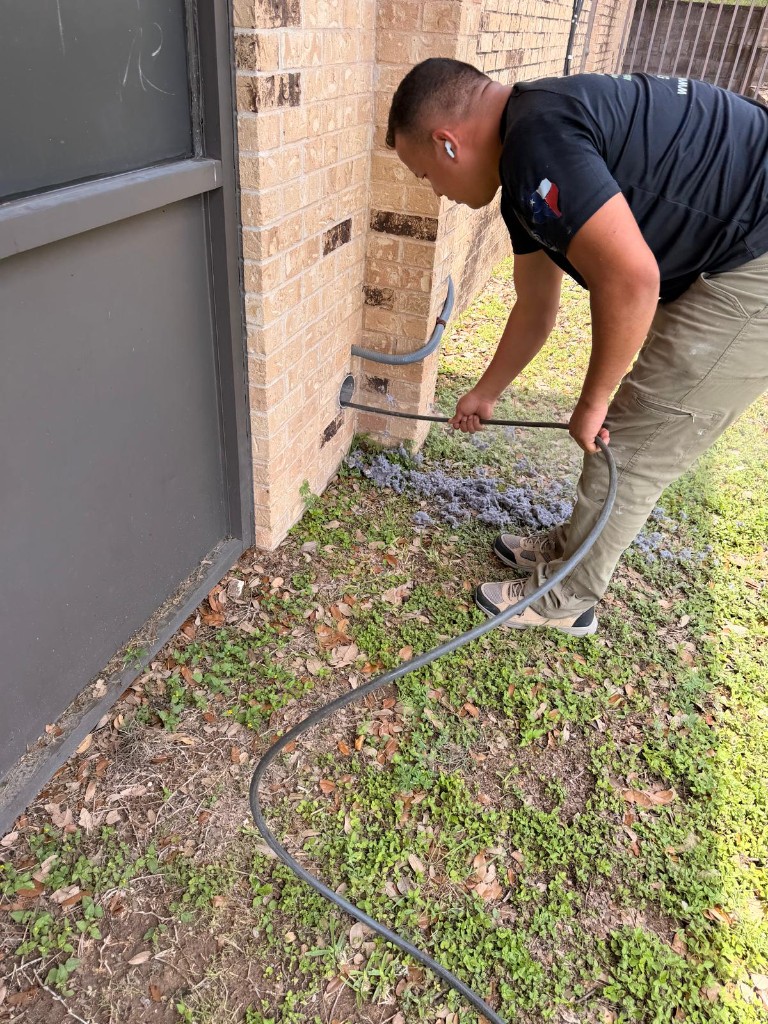 Technician feeding a cleaning hose into a brick-wall dryer vent with lint on the ground
