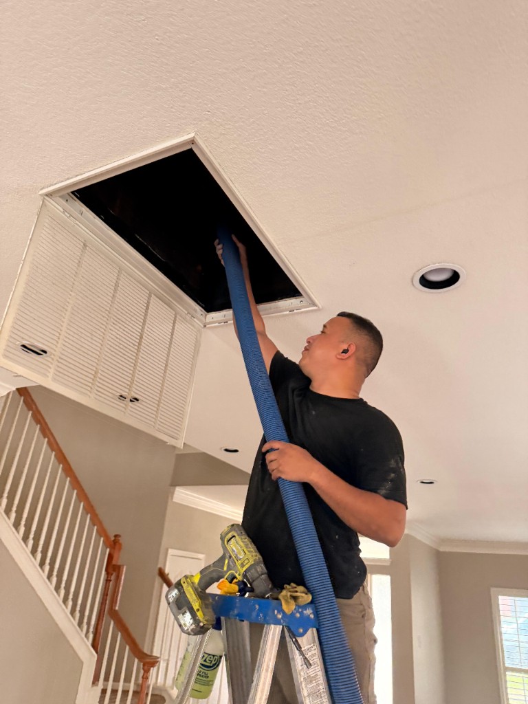 Technician on a stepladder feeding a blue hose into a ceiling duct